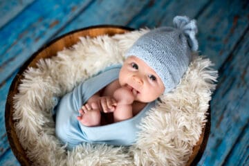 baby swaddled in a blue blanket with a blue cap resting in a basket