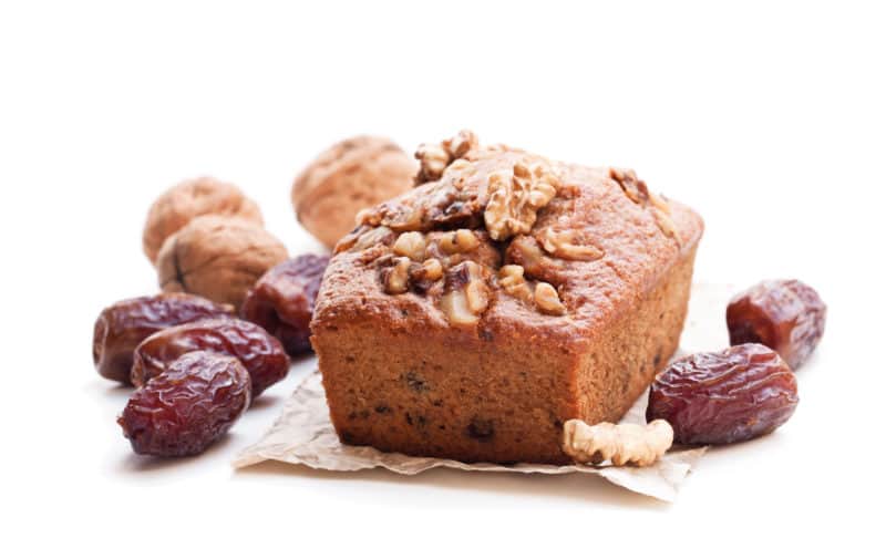Date-nut bread loaf surrounded by dates and walnuts in the shell