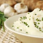 Garlic Mashed Potatoes in a bowl on a table next to fresh garlic and chives