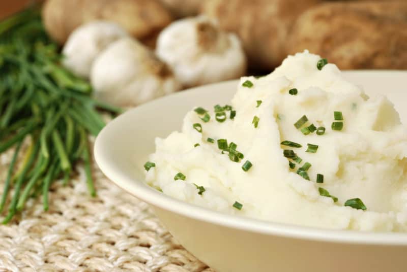 Garlic Mashed Potatoes in a bowl on a table next to fresh garlic and chives