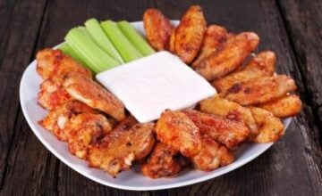 Buffalo chicken wings on plate with blue cheese sauce and celery.